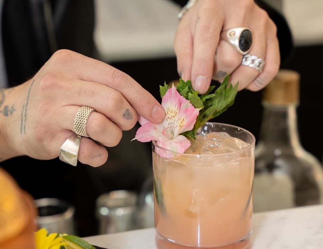 A bartender garnishing a pink cocktail with mint and a flower